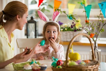 Mother and daughter celebrating Easter, eating chocolate eggs. Happy family holiday. Cute little girl in bunny ears laughing, smiling and having fun.