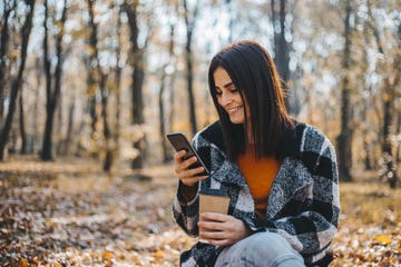 woman smiling and looking at her phone while holding a coffee