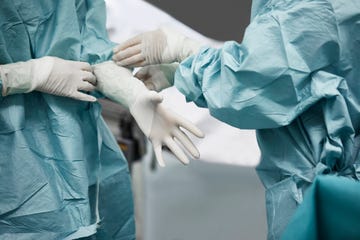 female doctor helping surgeon wearing glove