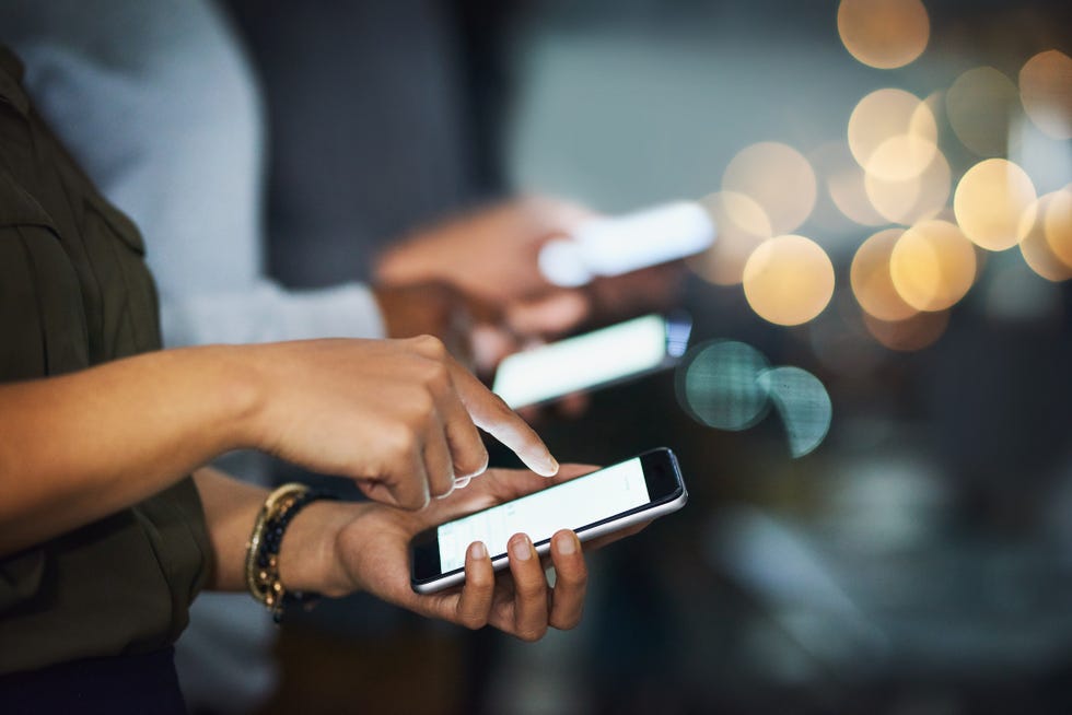 cropped shot of a group of unrecognizable businesspeople texting on their cellphones in the office at night