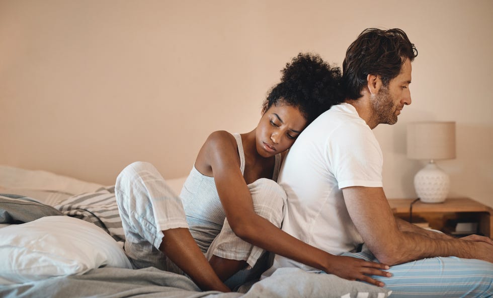 shot of a woman embracing her husband from behind while sitting in their bedroom