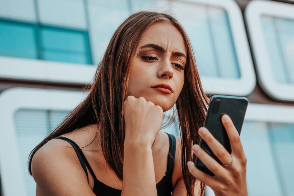 reading bad news on mobile phone young teenage woman checking her messages and social media post on her mobile phone looking worried and questioning reading the bad news and messages on her smart phone urban young generation social media lifestyle portrait