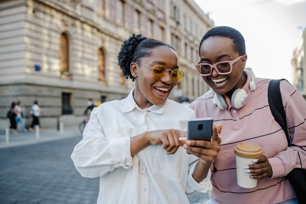 two young woman standing on the street and looking at the phone