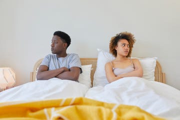 young couple on bed, they are looking away from each other and look irritated