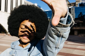 young afro woman with her eyes closed and smiling while covering herself from the sunlight with her hand