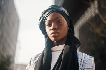 side view low angle of self assured african american muslim lady dressed in stylish checkered blazer with islamic headscarf and leather beret looking at camera with confidence