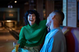 cheerful woman talking while having drink with male friend at bowling alley