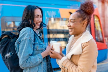 two women in a denim jacket is talking to each other , drinking coffee and waiting for a tram at the stop lifestyle photo