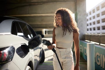 young woman with curly hair holding electric plug by car at charging station