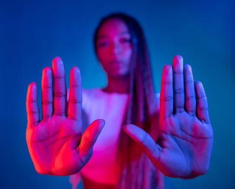 a woman dancing and using her hands with the palms facing the camera for a stop gestures against a blue background focus on foreground