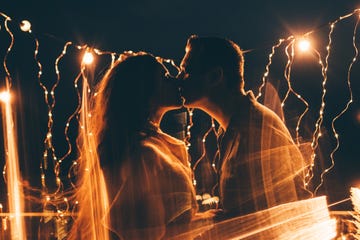 bride and groom kissing near the wedding arch at night with lights, silhouettes of the newlyweds