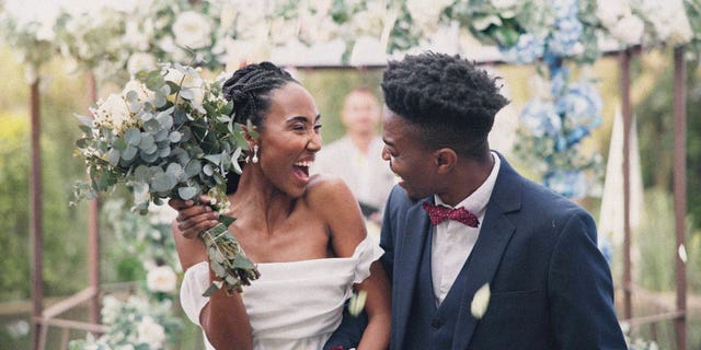 couple, flower confetti and outdoor wedding with event, walk and happy laugh in nature black woman, man and excited for marriage, floral bouquet or holding hands in park, party or together in aisle