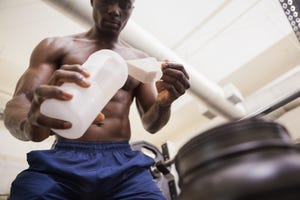 shirtless body builder scooping up protein powder in gym