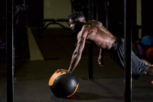 man doing push ups with a weight ball inside a gym with a black floor healthy life concept