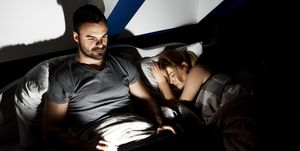 High Angle View Of Man Using Laptop While Woman Sleeping On Bed