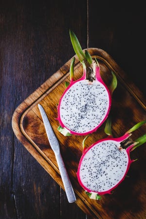 high angle view of pitaya with knife and cutting board on wooden table