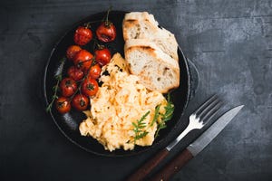 scrambled eggs and oven roasted cherry tomatoes with toasted bread in rustic cast iron skillet viewed from above