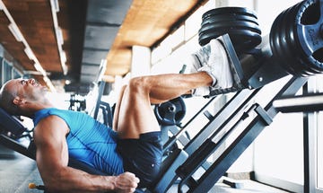 closeup side view of late 20's muscular man doing a leg press exercise at a gym he's wearing blue sleeveless shirt and black trunks