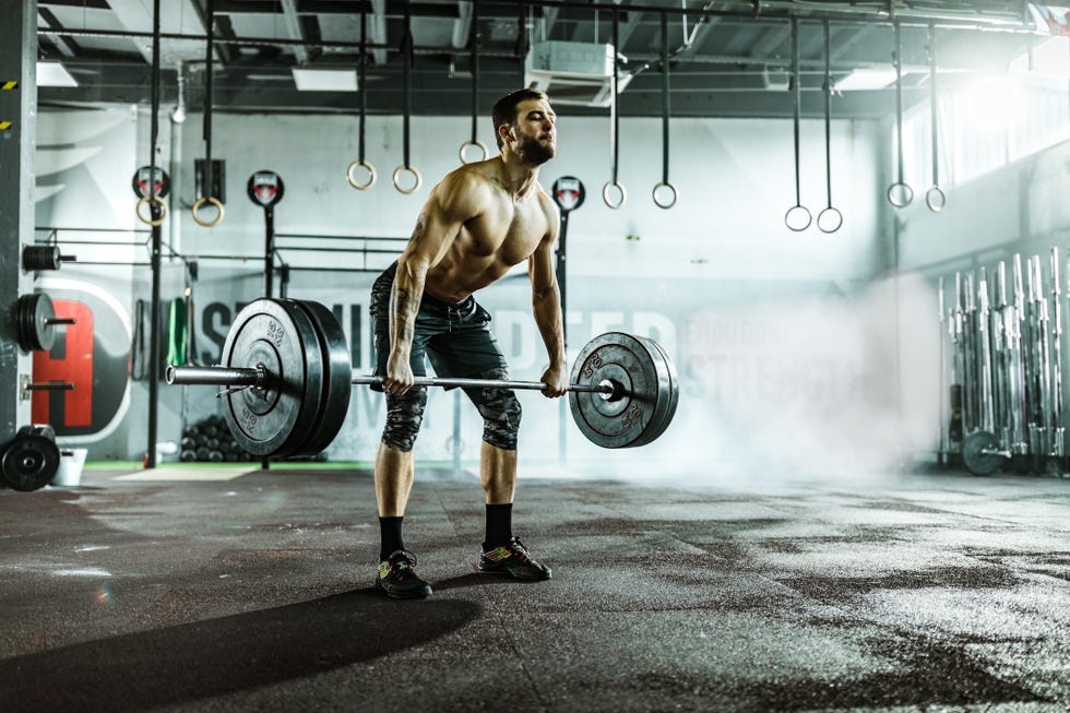 Male athlete making an effort while lifting barbell in a gym.