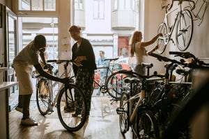 male owner repairing bicycle of senior customer while colleague working on bike at workshop