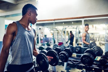 cropped shot of a handsome young athletic man watching himself in the mirror while working out with dumbbells in the gym