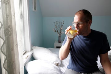 man sitting on side of bed, drinking water with lemon, side view