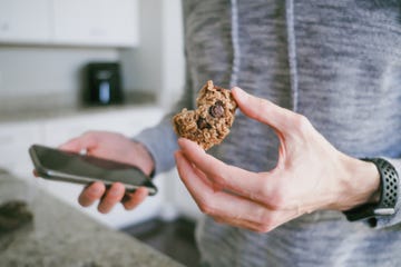 man snacks on cookie while looking at his smart phone