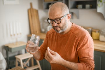 mature adult man in cozy interior of home kitchen  taking medication