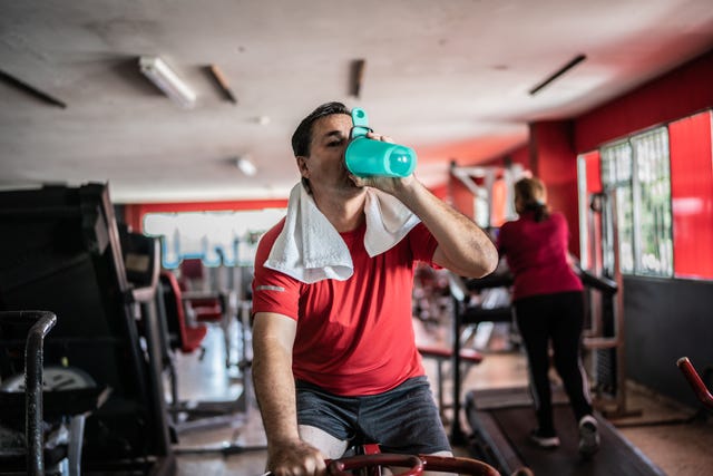 mature man using exercise bicycle and drinking water at a gym