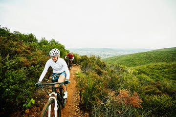 mature woman climbing hill while riding mountain bike on trail with husband