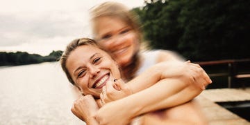 two white women laughing on a beach one has their face blurred and arms around the woman who is clearly in focus