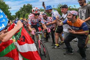 a cyclist in a polka dot jersey riding up a hill through a crowd of cheering spectators