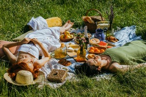 a person lying on the grass next to a cat and basket of food