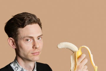 portrait of a mid adult man holding banana over colored background