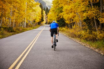 rear view of senior man riding bicycle on country road in forest