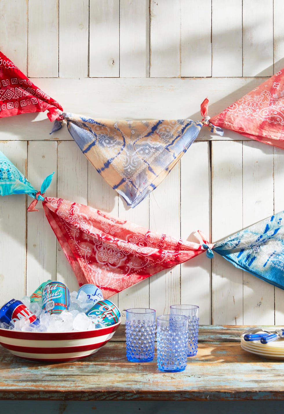 tie dye bandanas tied together in a bunting hung on a white wall in front of a table