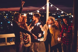 couple of friends having a party on the rooftop of the building at sunset drinking bottles of beer and holding sparklers wearing knitted sweaters, hats and scarfs they are happy and joyful