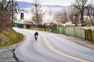 a person riding a bicycle on a road with a fence and trees