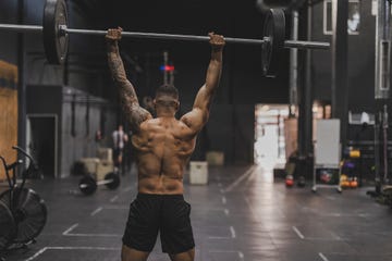shirtless man in gym lifting dumbbells back