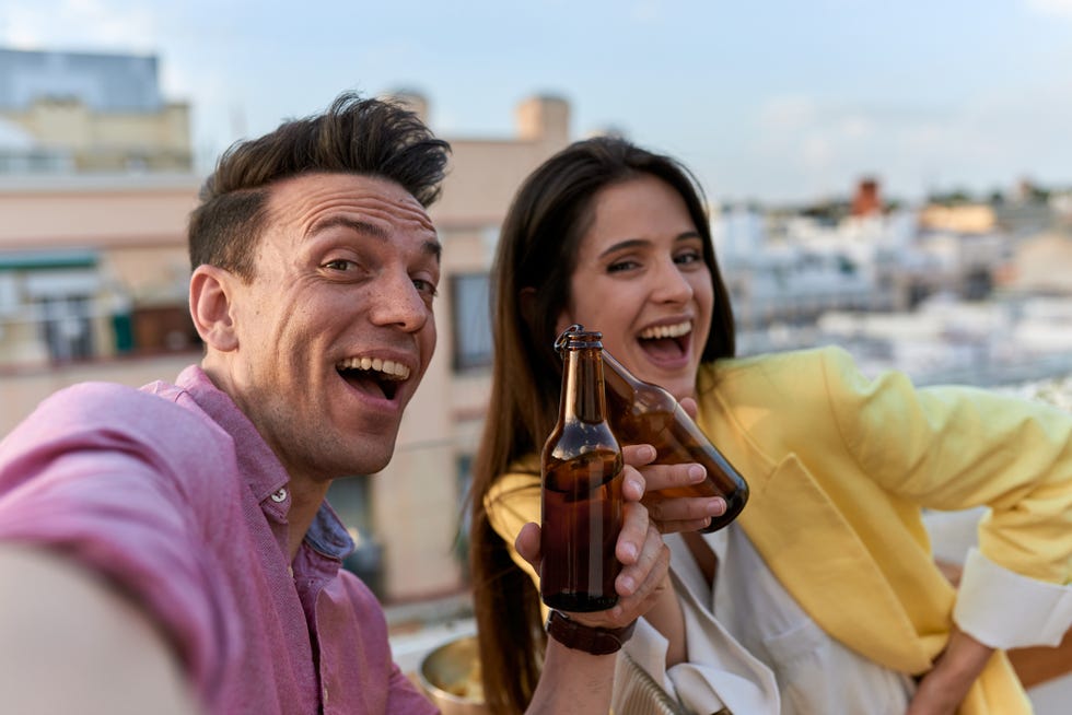 happy couple smiling and taking selfies while enjoying drinking beer outdoors siblings