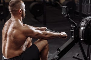 side view photo of shirtles man using th rowing machine while training