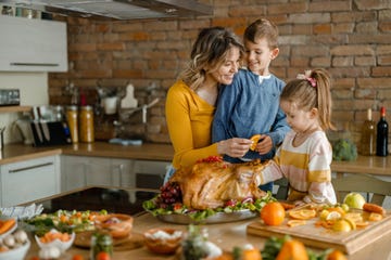 happy single mother and her small kids decorating turkey on thanksgiving day in the kitchen