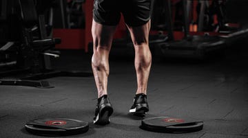 trained man's legs with muscular calves in sneakers in fitness training gym