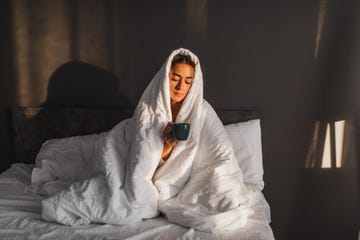 woman wrapped in blanket in bed holding a hot drink