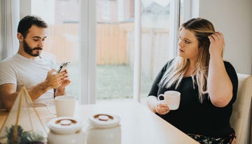 a woman looks insecure as her partner ignores her to look at his phone