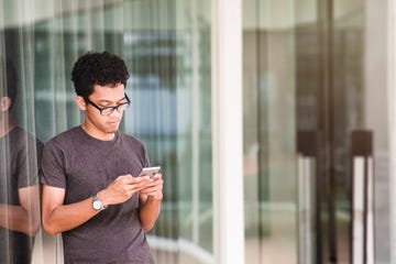 young asian man text messaging outdoors in urban setting