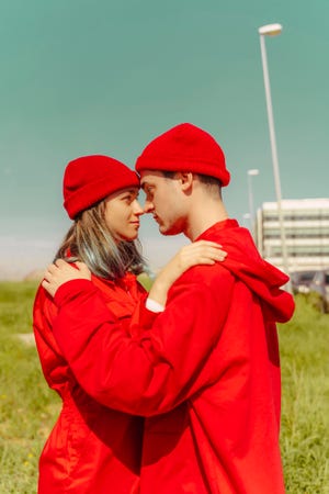 young couple wearing red overalls and hats standing head to head looking at each other