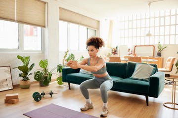 young fit woman doing squats in living room