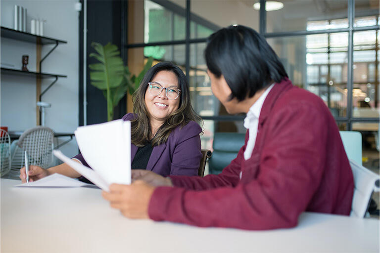 Two colleagues sit at a desk, smiling, as they complete their Achieve Together meeting.