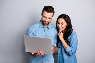 Casal vestindo jeans utiliza notebook na frente de uma parede cinza